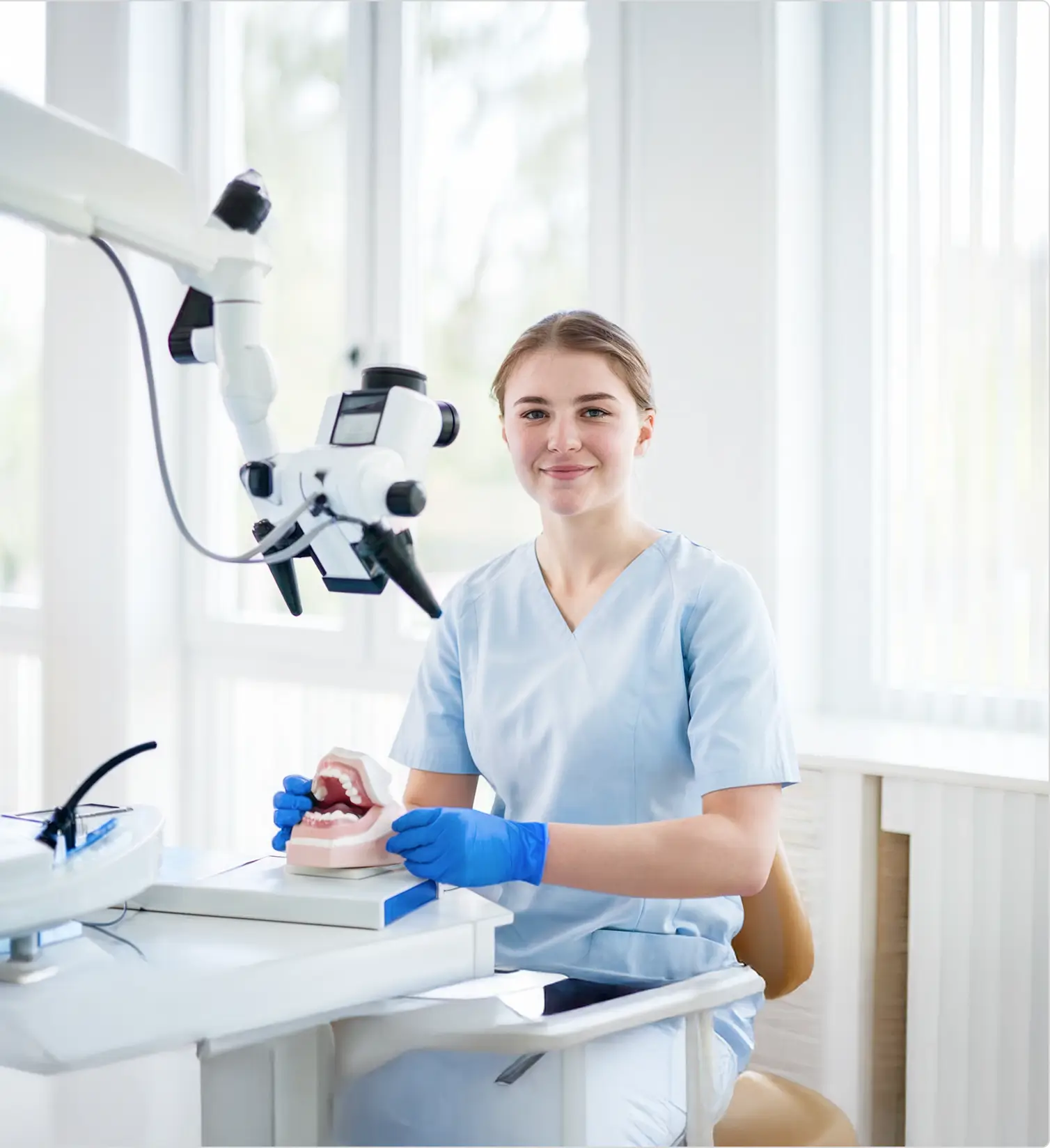 Dental professional holds a dental model beside a microscope.