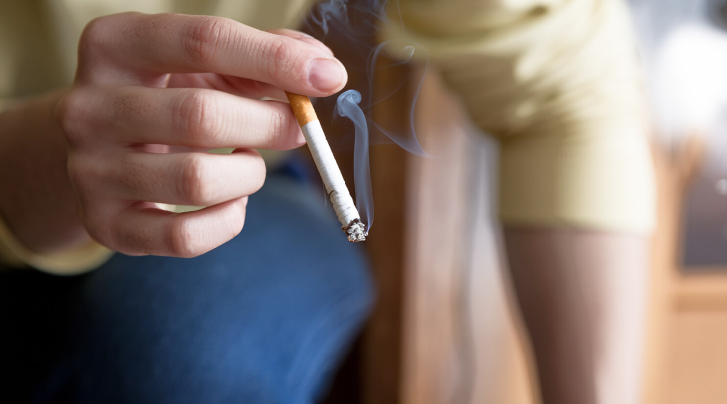Person holding a lit cigarette with visible smoke rising from the tip.