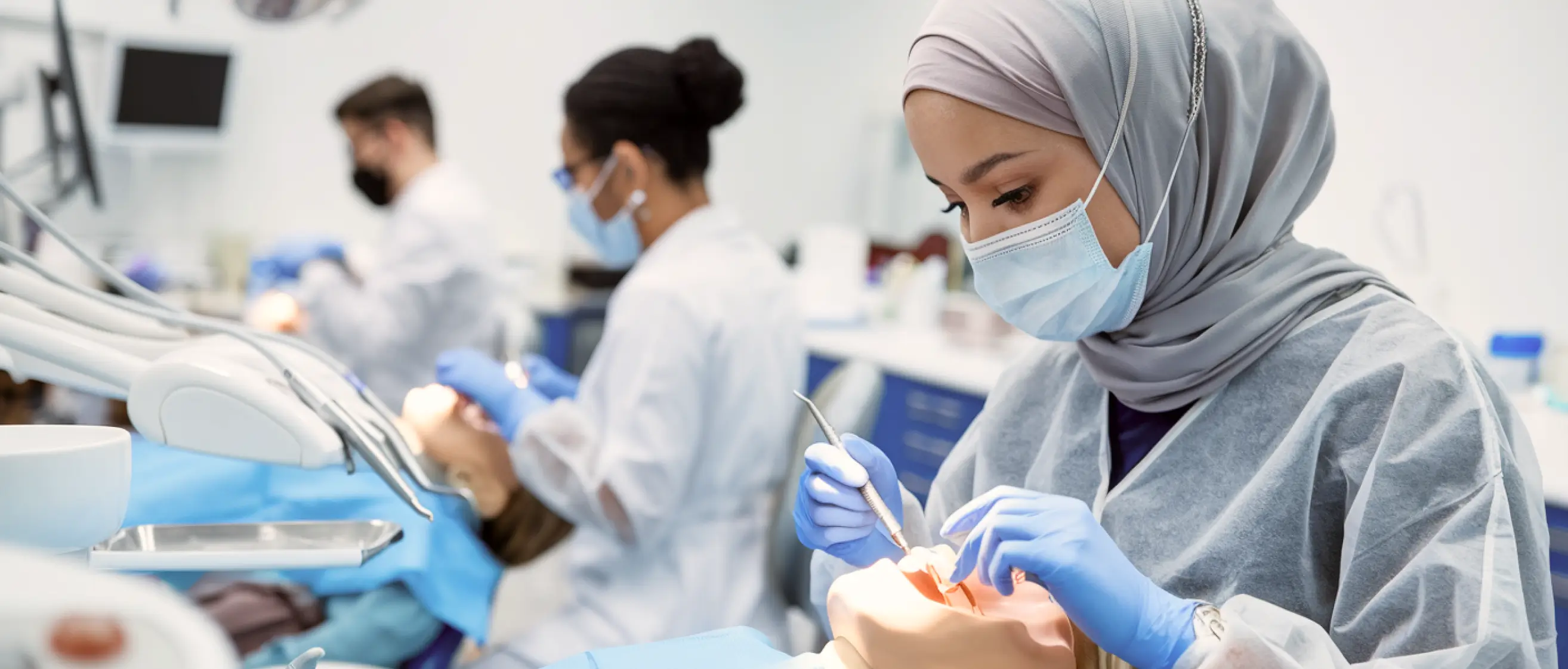 Dental students wearing masks practice procedures in a clinical training lab.