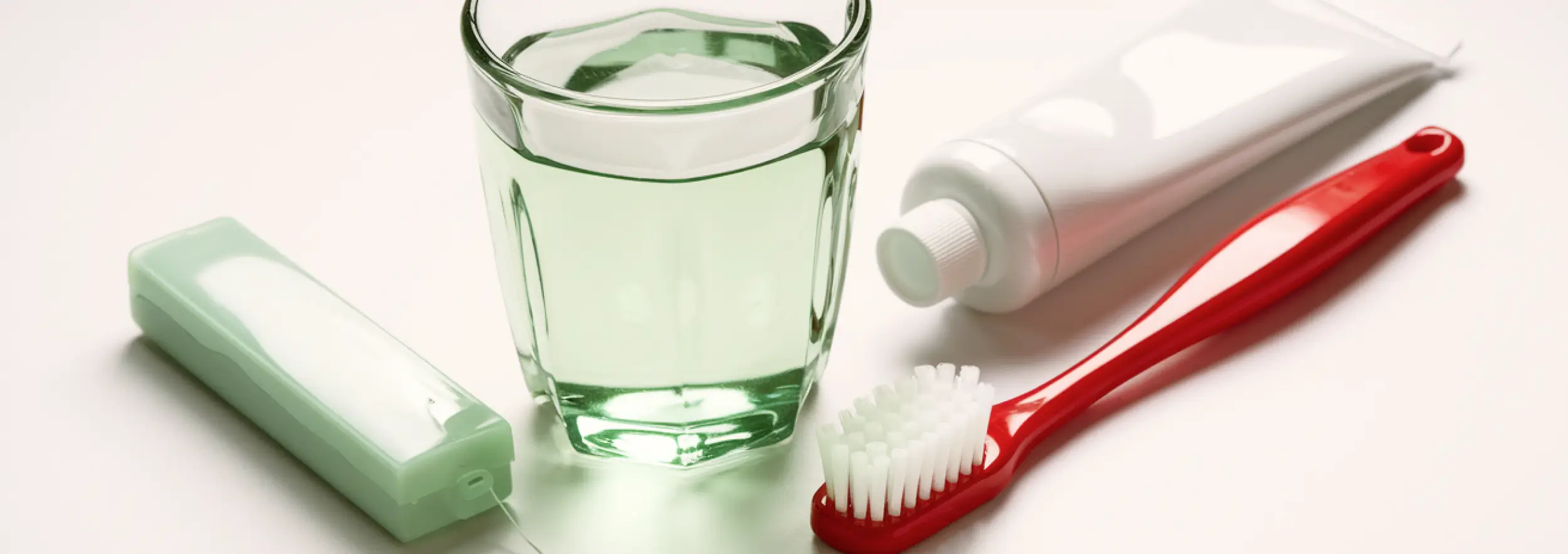Toothbrush, toothpaste, dental floss, and mouthwash on a white surface